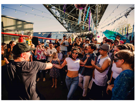 People dance under hanging lights at twilight on Granville Island